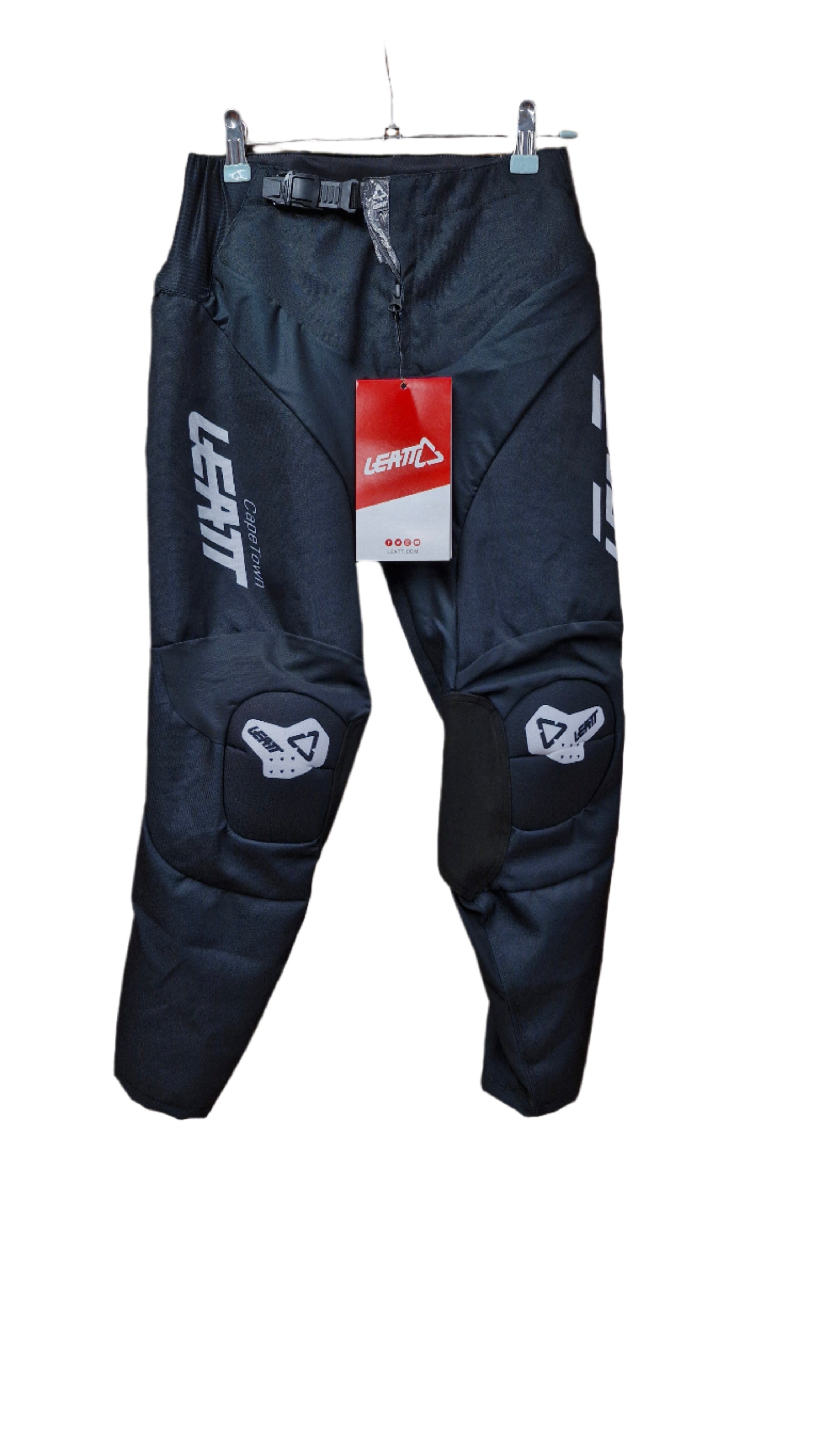 A pair of black Leatt GPX 3.5 motorcycle pants for juniors displayed against a wooden background, with the brand tag visible.